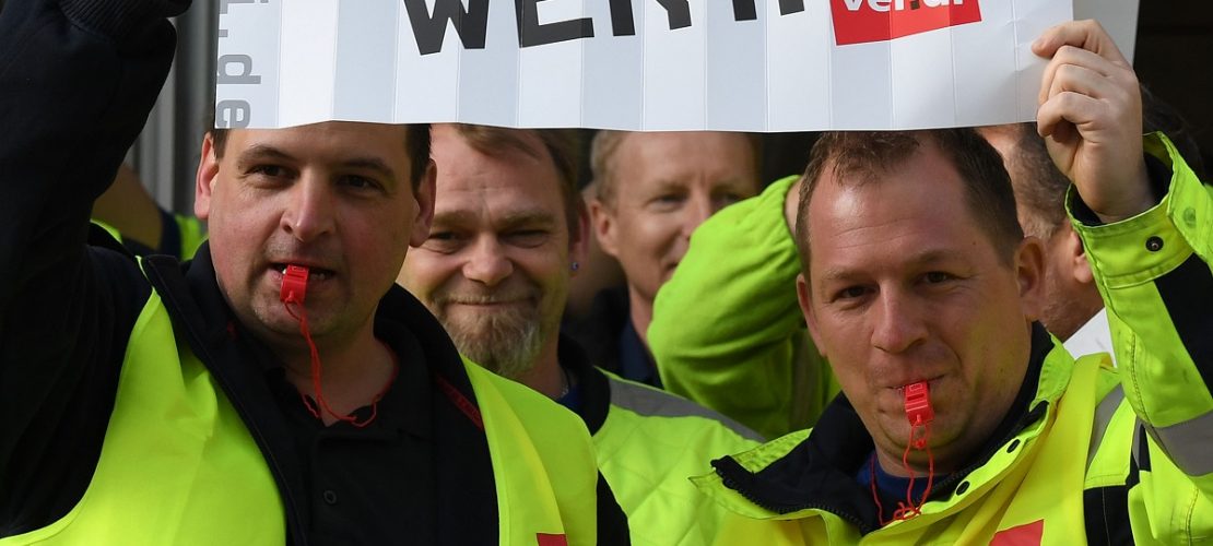 10.04.2018, Bremen: Streikende ver.di Mitarbeiter stehen vor einem Eingang zum Airport Bremen und halten Plakate mit 